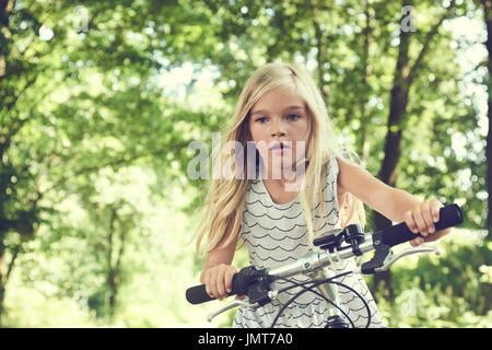 Enfant fille blonde de rouler à vélo sur une piste cyclable en été Banque D'Images