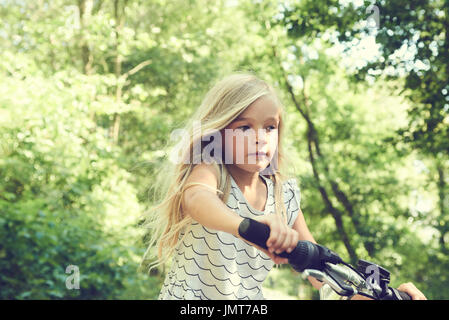 Enfant fille blonde de rouler à vélo sur une piste cyclable en été Banque D'Images
