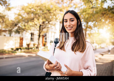 Young hispanic female student avec réserve en collège. Belle jeune femme avec livre sur la route. Banque D'Images