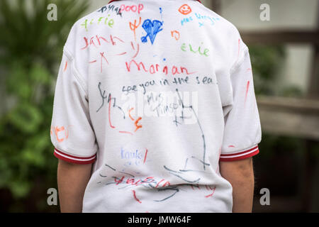 Un jeune élève de l'école Junior portant une chemise blanche signée par tous ses amis à la fin de l'école d'été. Newquay, Cornwall. Banque D'Images