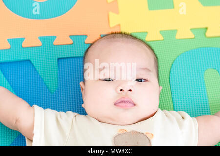 Portrait d'un adorable petit bébé fille bébé allongé sur le dos sur mousse eva colorés et à la recherche à l'intérieur de l'appareil photo Banque D'Images