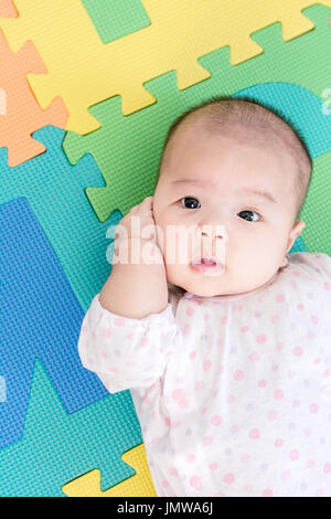 Portrait d'un adorable petit bébé fille bébé allongé sur le dos sur mousse eva colorés et à la recherche à l'intérieur de l'appareil photo Banque D'Images