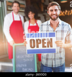 Portrait de l'homme propriétaire holding open sign smiling collègues posant derrière un tableau Banque D'Images