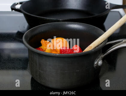Décisions d'abricot et de gelée de fraises dans une casserole anti-adhérente sur le dessus d'une cuisinière électrique Banque D'Images