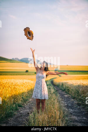 Jeune femme heureuse dans un champ de blé avec robe blanche et chapeau d'été Banque D'Images