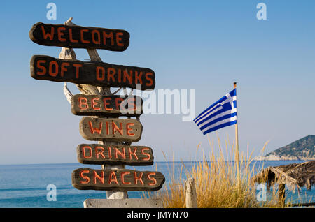 Panneaux en bois sur la plage indiquent la présence d'un bar proposant des aliments et boissons à Skiathos, Grèce, sur le fond le drapeau grec Banque D'Images