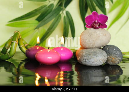 Cailloux disposés en style Zen sur la droite avec une orchidée en haut et allumé des bougies rose Banque D'Images