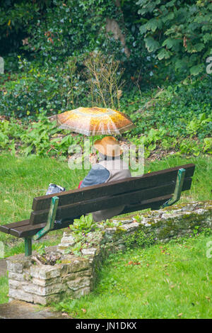 Bournemouth, Dorset, UK. 29 juillet, 2017. Météo France : la pluie ne s'arrête cette femme assise dans un parc sous son parapluie de quelque chose à manger à Robert Louis Stevenson gardens Skerryvore dans Westbourne, Bournemouth. Credit : Carolyn Jenkins/Alamy Live News Banque D'Images