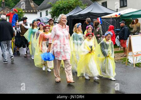 Milton Abbas, Dorset, UK. 29 juillet 2017. Les fortes pluies ne parvient pas à décourager les visiteurs, dont le troupeau à la Milton Abbas Foire de rue 18e siècle dans le Dorset. Ancien journaliste de BBC News Kate Adie marcher dans la procession dans la rue du village avec des enfants à partir des étapes dans le temps après l'ouverture de la foire. Crédit photo : Graham Hunt/Alamy Live News Banque D'Images