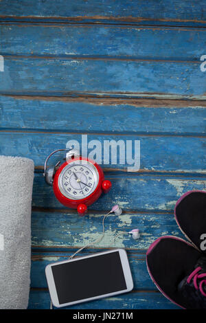 Vue de dessus de réveil par téléphone mobile au milieu de nappes et des chaussures de sports sur table en bois bleu Banque D'Images