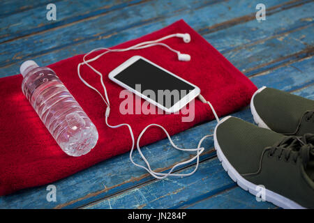 Portrait de l'eau bouteille avec téléphone mobile et mini-écouteurs sur nappes par les chaussures de sports sur table en bois bleu Banque D'Images