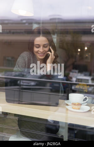Smiling Woman talking on phone in cafe vu à travers la vitre Banque D'Images