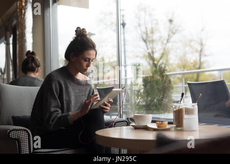 Woman using digital tablet while sitting on armchair in cafe Banque D'Images