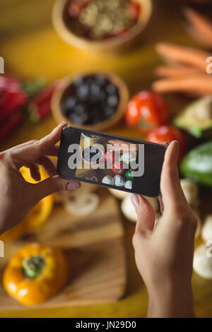 Woman taking photo de légumes biologiques avec mobile phone in kitchen Banque D'Images