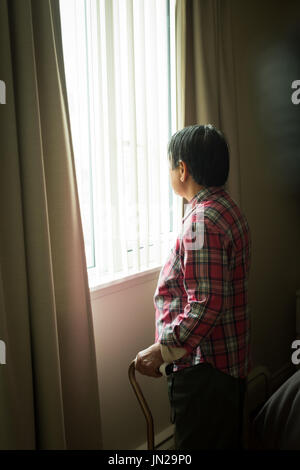 Vue latérale du senior woman standing by window at home Banque D'Images