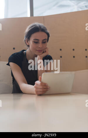 Femme propriétaire using digital tablet while sitting at table in cafe Banque D'Images