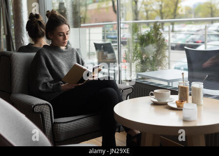 Young woman reading book, assis sur un fauteuil en cafe Banque D'Images