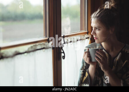 Thoughtful woman having coffee près de la fenêtre à la maison Banque D'Images