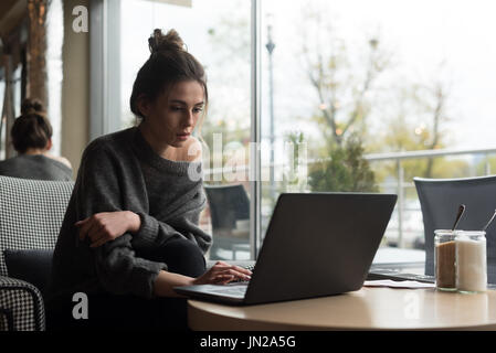 Young woman using laptop while sitting on armchair in cafe Banque D'Images