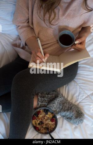 Vue de dessus de woman writing journal pendant le petit-déjeuner on bed Banque D'Images