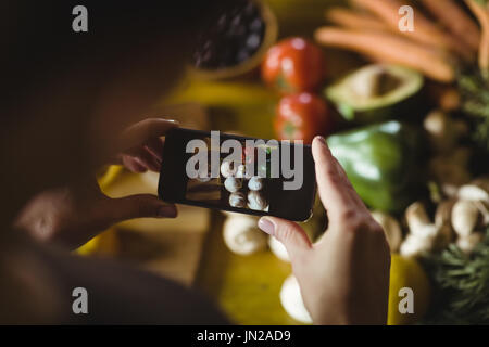 Woman taking photo de légumes biologiques avec mobile phone in kitchen Banque D'Images