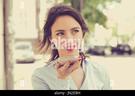 Femme à l'aide d'un smart phone fonction reconnaissance vocale en ligne marche sur une rue de ville un jour d'été Banque D'Images