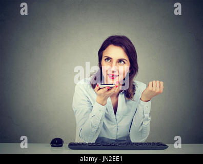 Femme à l'aide d'un smart phone fonction reconnaissance vocale à la ligne sitting at table isolé sur fond de mur gris Banque D'Images