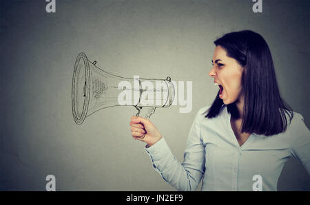 Portrait femme en colère crier dans un mégaphone isolé sur fond de mur gris. L'expression des sentiments négatifs face à l'émotion. Banque D'Images