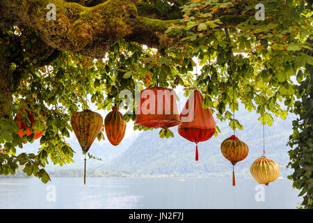 Lanternes traditionnelles asiatiques colorés (commun en Chine, Corée, Japon, Vietnam, Thaïlande) accroché au-dessous d'un vieil arbre avec des feuilles vertes contre un lac. Banque D'Images