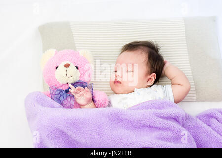 Portrait de bébé endormi sur un lit de poupée ours Banque D'Images