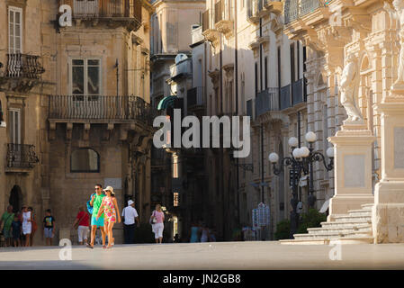 Couple Italie Ville, vue d'un jeune homme et femme sur la maison de marche à travers une piazza dans Ortigia, Sicile, en Italie. Banque D'Images