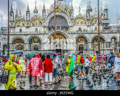 Basilique-cathédrale Saint Marc à Venise Italie un jour de pluie encombrée de touristes dans les imperméables et les parapluies colorés comme les pigeons à pied autour de Banque D'Images