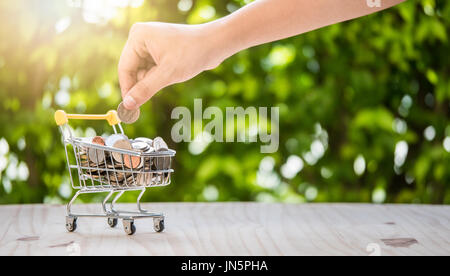 Hand holding coin mettre dans votre panier sur la table de bois avec bokeh background en concept commercial ou financier Banque D'Images