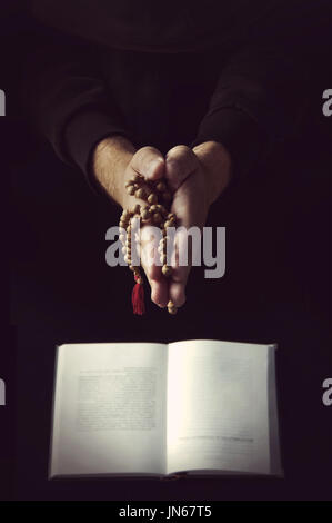 Hands holding rosary et plié dans la prière sur un fond noir. Banque D'Images