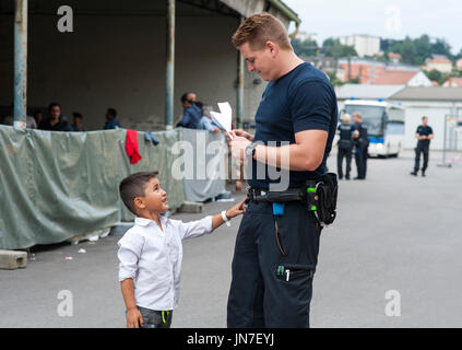 Agent de police avec un jeune garçon des réfugiés syriens au centre d'inscription à Passau, Allemagne. Le préposé communique avec le petit garçon. Banque D'Images