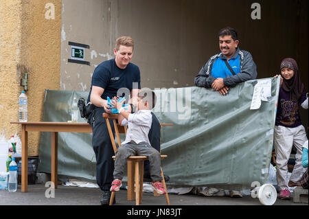 Passau, Allemagne - 1 août 2015 : un officier de police allemand prend soin d'un petit enfant réfugié dans la zone d'enregistrement de Passau. Banque D'Images