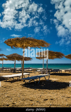 L'île de Paros, Cyclades, en Grèce. Des parasols de paille et des chaises longues sur la plage dorée. Banque D'Images