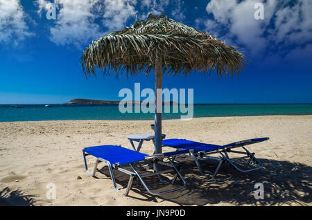 L'île de Paros, Cyclades, en Grèce. Des parasols de paille et des chaises longues sur la plage dorée. Banque D'Images