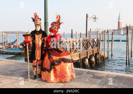 Février 2107 Venise, Vénétie, Italie. En couple classique coloré orange Carnival costumes et des masques posant au lagoon à Piazza San Marco avec Banque D'Images