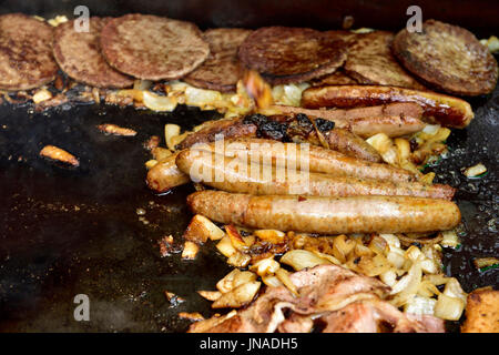 Des saucisses, des hamburgers, du bacon et des oignons cuits sur une plaque chauffante Banque D'Images