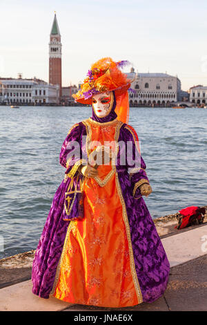 Carnaval de Venise 2017, Venise, Vénétie, Italie. Femme en classique coloré costume orange et violet posant sur San Girogio Maggiore avec les Doges Pal Banque D'Images