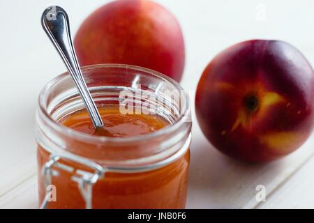 Pot en verre de pêche et/ou de la confiture de nectarine avec une cuillère en contre fond blanc Banque D'Images