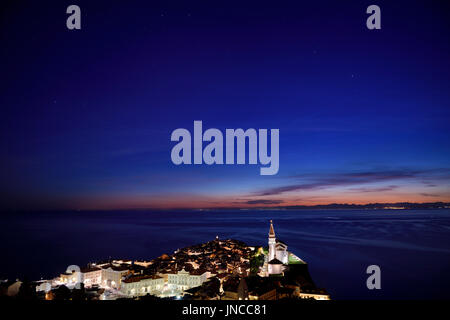 Stars sur Piran Slovénie la nuit avec la place Tartini Courthouse Hôtel de Ville et la cathédrale St George avec des lumières de distance en Italie Banque D'Images