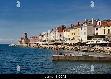 Jeune couple pêche à la lecture de soleil sur dock à Piran Slovénie sur la côte de la mer Adriatique à l'église de St Clement au phare de Punta Banque D'Images