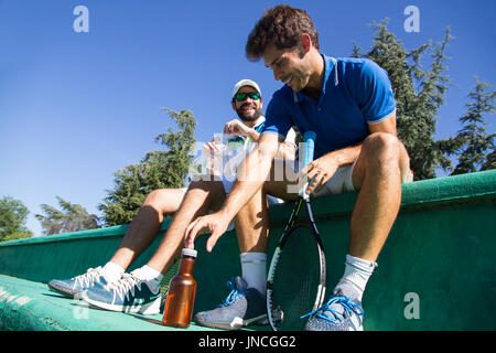 Deux joueurs professionnels hydrater après une partie de tennis. Ils sont amis et sont assis en appui pour le jeu. Ils sont heureux et rire. Banque D'Images