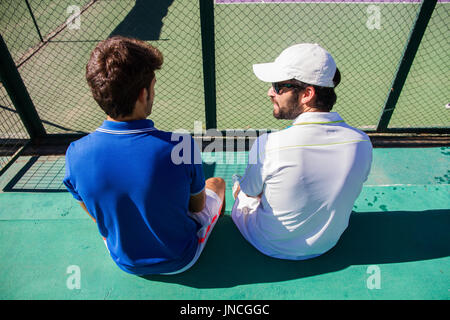 Deux joueurs professionnels se reposant après une partie de tennis. Ils sont amis et sont assis en appui pour le jeu. Ils sont heureux et rire. Banque D'Images