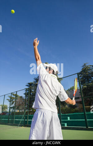 Joueur de tennis est en train de faire un coup de tennis sur un court de tennis sur un matin d'été ensoleillé. Il est vêtu de vêtements de sport. Banque D'Images