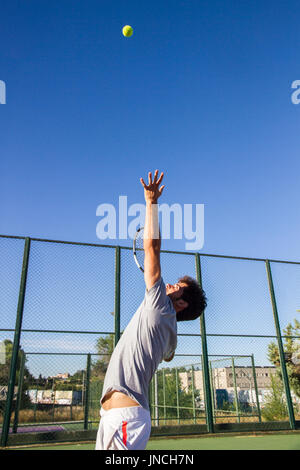 Joueur de tennis est en train de faire un coup de tennis sur un court de tennis sur un matin d'été ensoleillé. L'est habillé en vêtements de sport. Banque D'Images