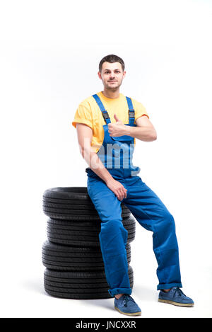 Conscrit dans l'uniforme bleu assis sur pneumatiques, fond blanc, réparateur de pneus Banque D'Images