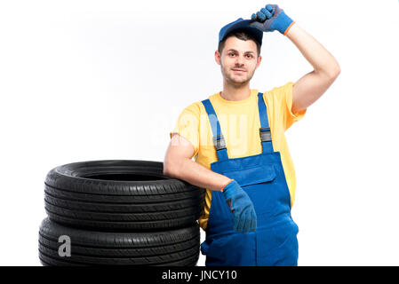 Conscrit dans l'uniforme bleu assis sur pneumatiques, fond blanc, réparateur de pneus Banque D'Images